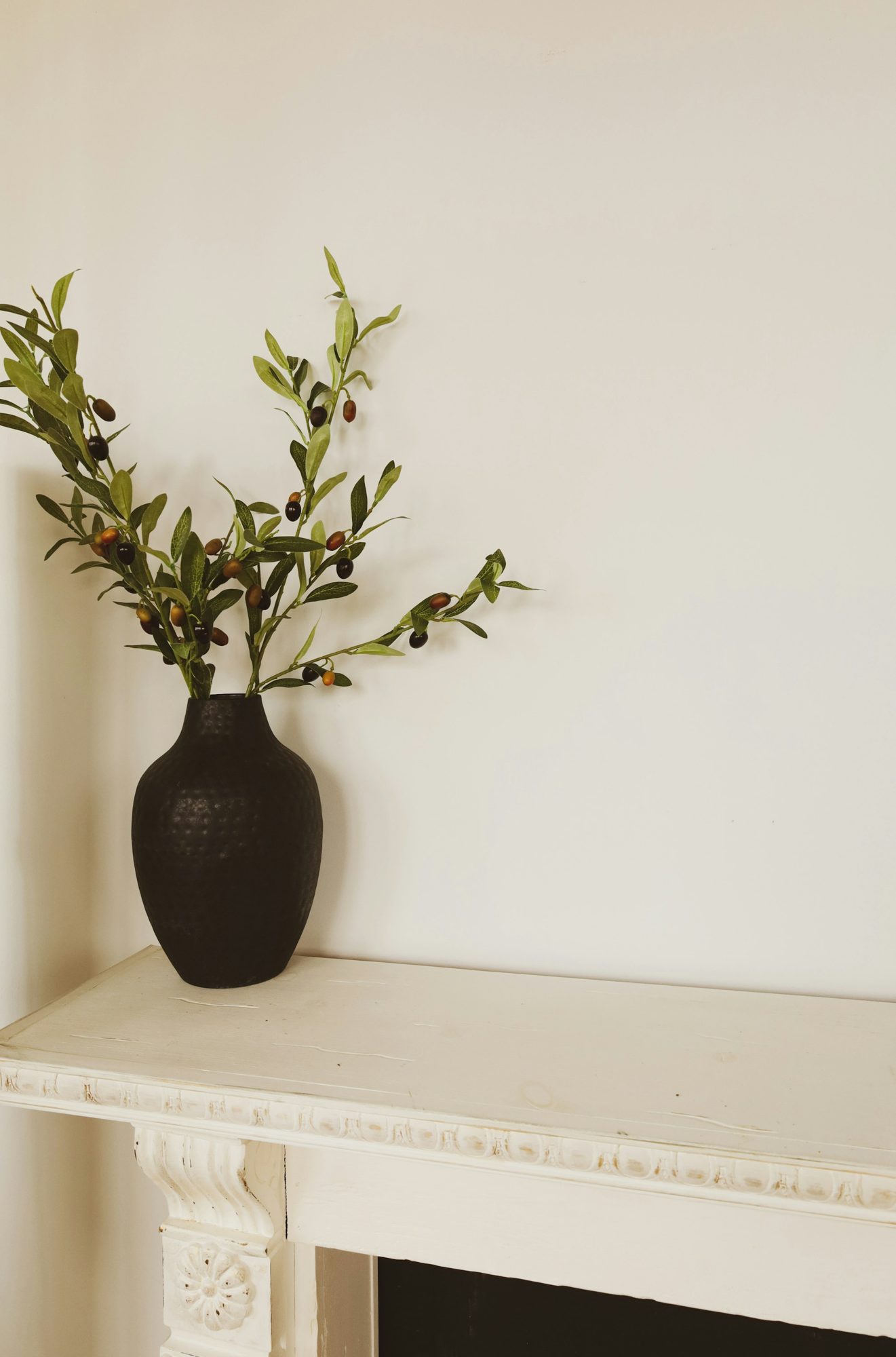 An olive branch in a black vase on a white mantel